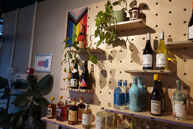 Wall with a variety of drinks bottles shelved on it along with plants